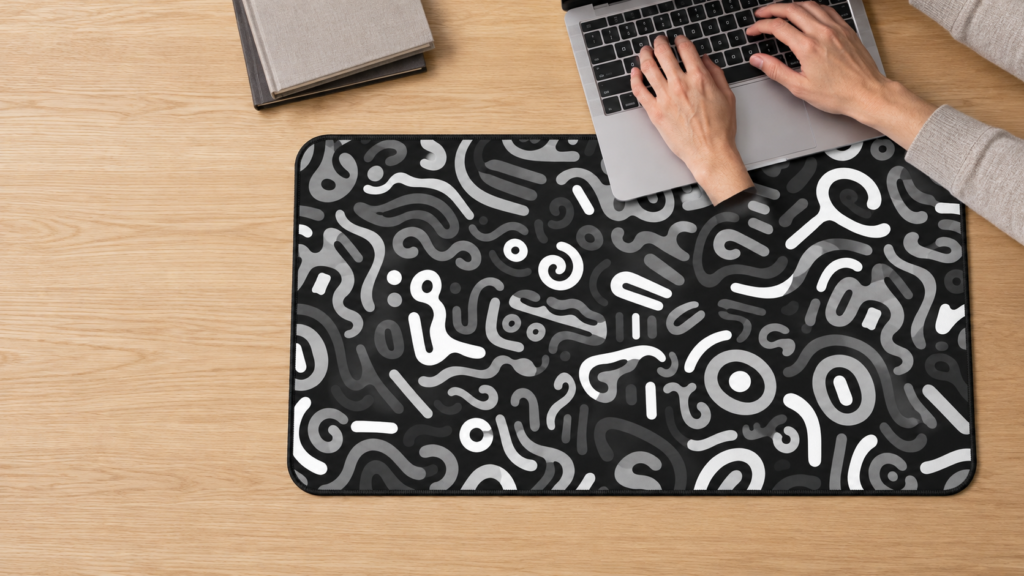 Black and white abstract desk mat with a person working on a laptop and books nearby.